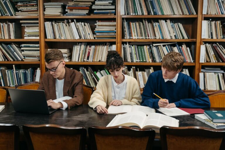 Students studying with laptops and books in a university library, using AI tools for learning