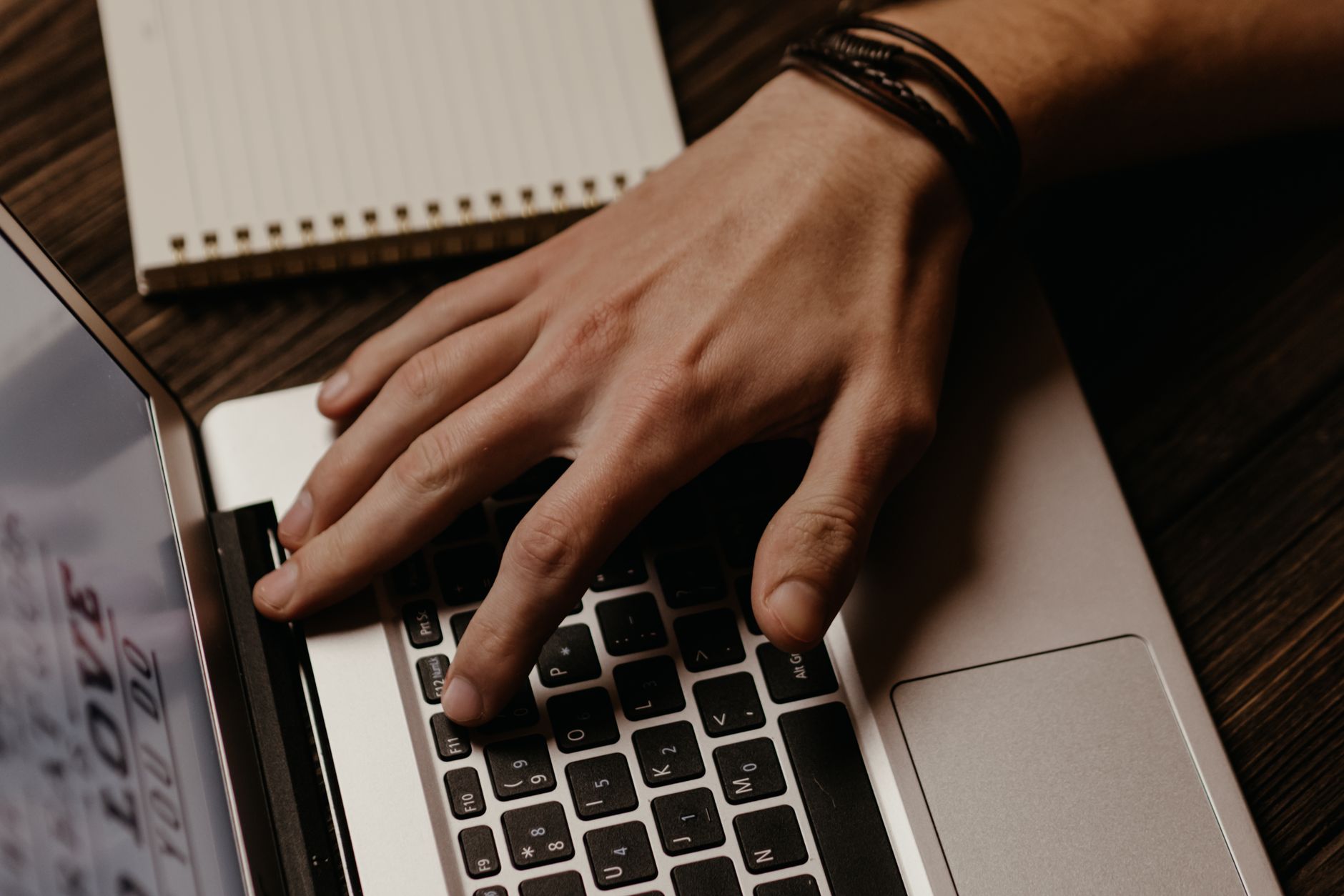 Hand typing on a laptop keyboard with a notebook nearby, illustrating AI writing tools for bloggers and content creators