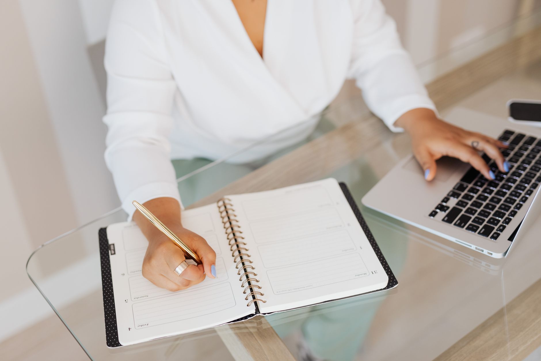 Content creator writing notes in a planner notebook while working on a laptop