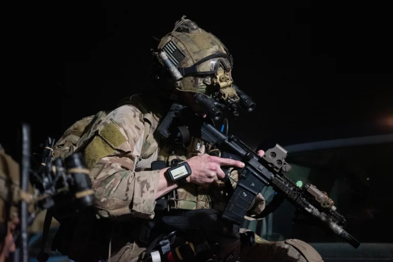 A U.S. Air Force Special Tactics Airman checks his equipment in full tactical gear during a nighttime training scenario