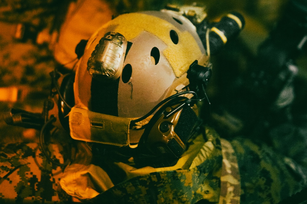 U.S. Marines and allied troops prepare tactical gear under amber lighting before a nighttime training exercise