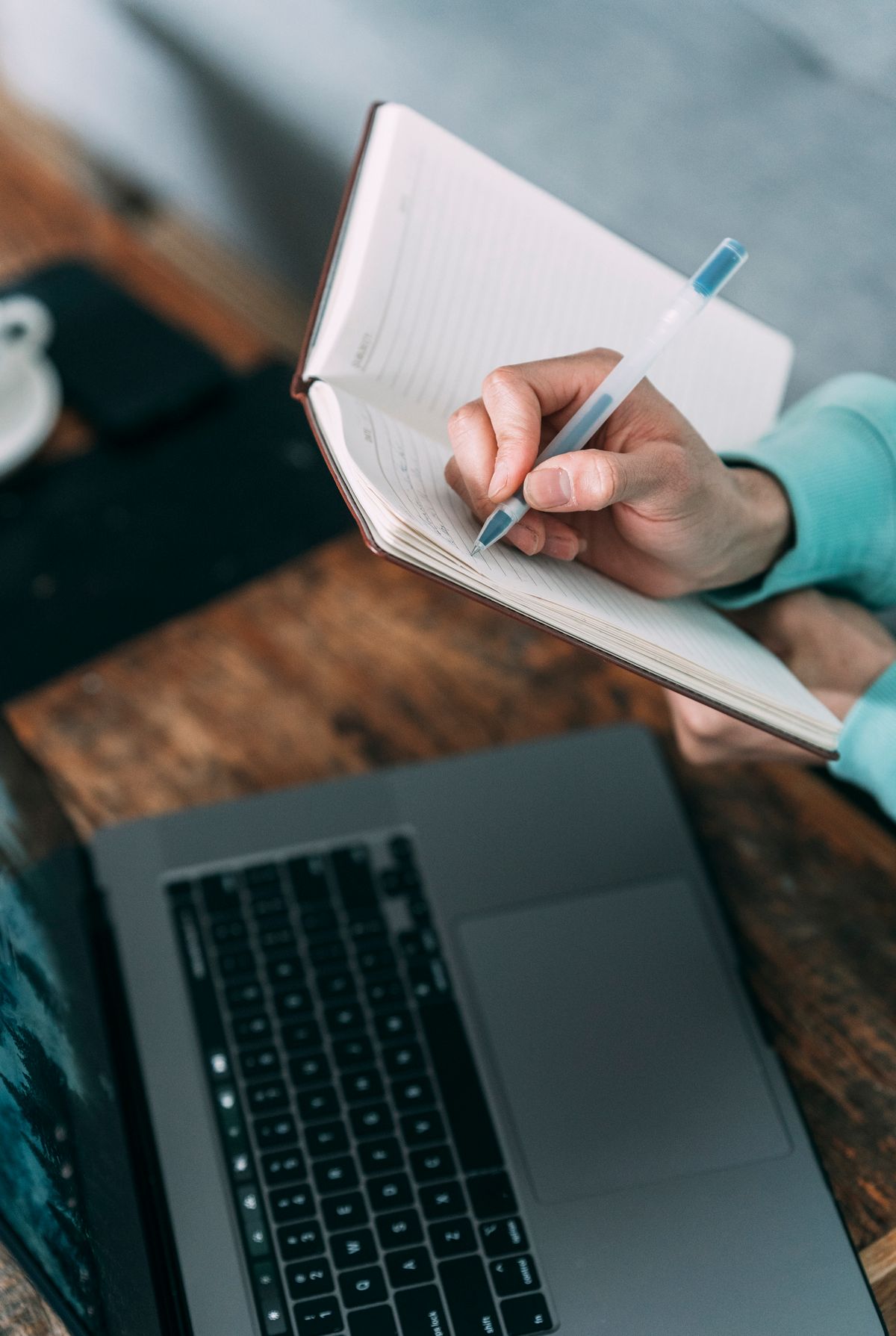 Overhead view of a person taking notes in a notebook next to a laptop on a desk