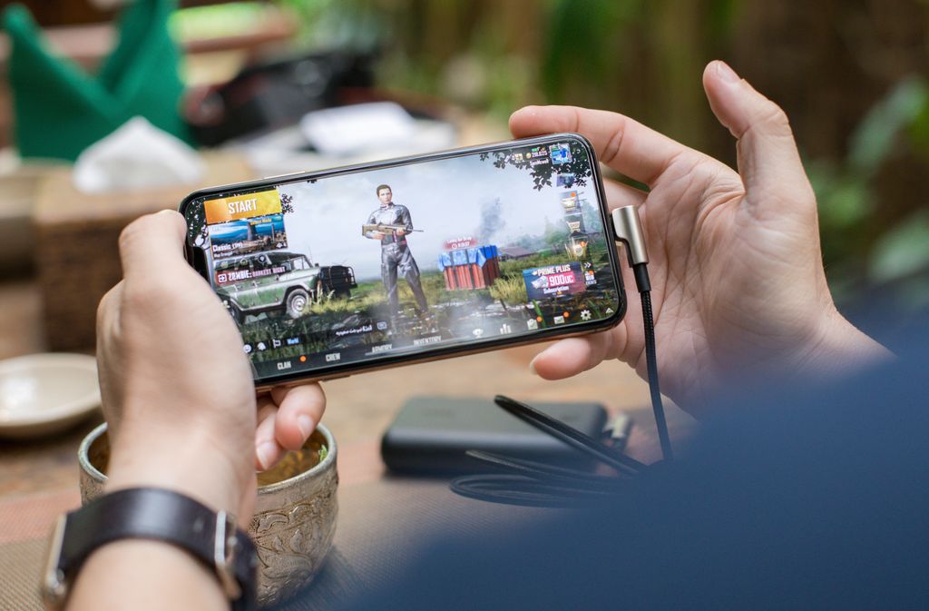 Person playing a mobile game on a smartphone outdoors with a charging cable attached
